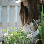 A woman in a hat watering flowers in a garden
